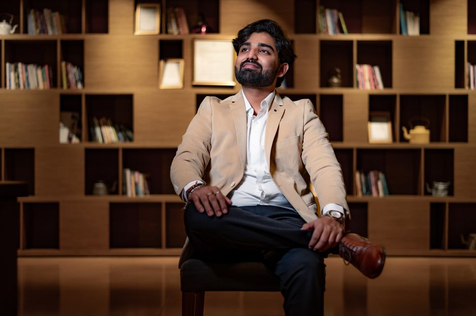 Portrait of a confident man seated in a stylish home library with warm lighting.